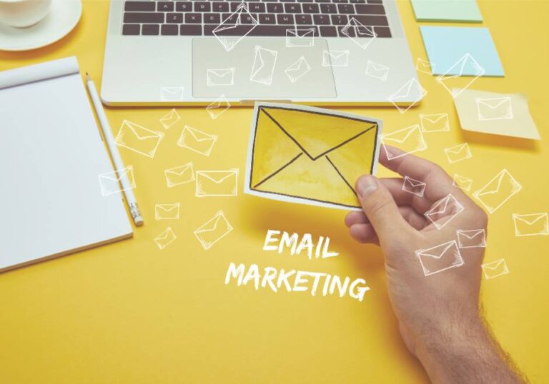 hand holding a paper cutout of envelope with email marketing written below a laptop